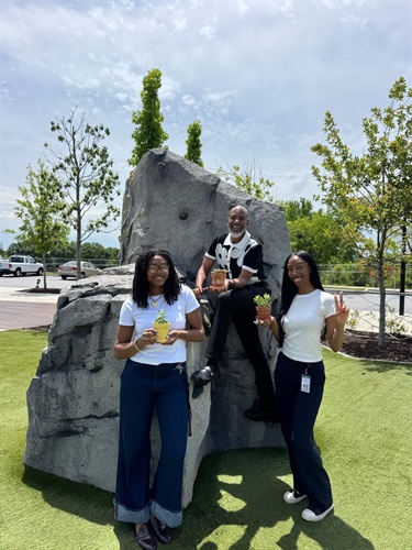 2 young ladies flank a young man in front of the climbing wall at the Town Green