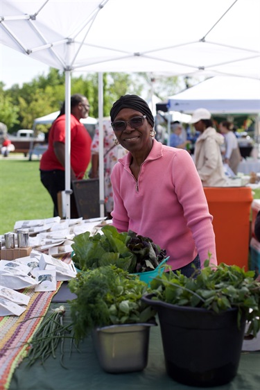Vendor at the Church St Farmers Market smiles in her booth behind plants for sale