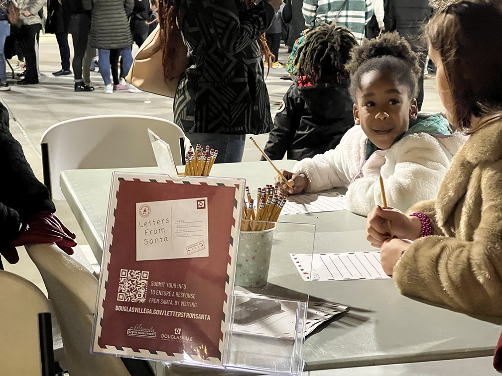 Young girl writes letter to Santa as her mother watches